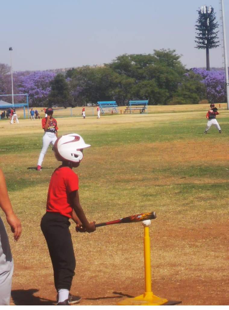 Young Tinashe at the batting tee in an oversized white helmet